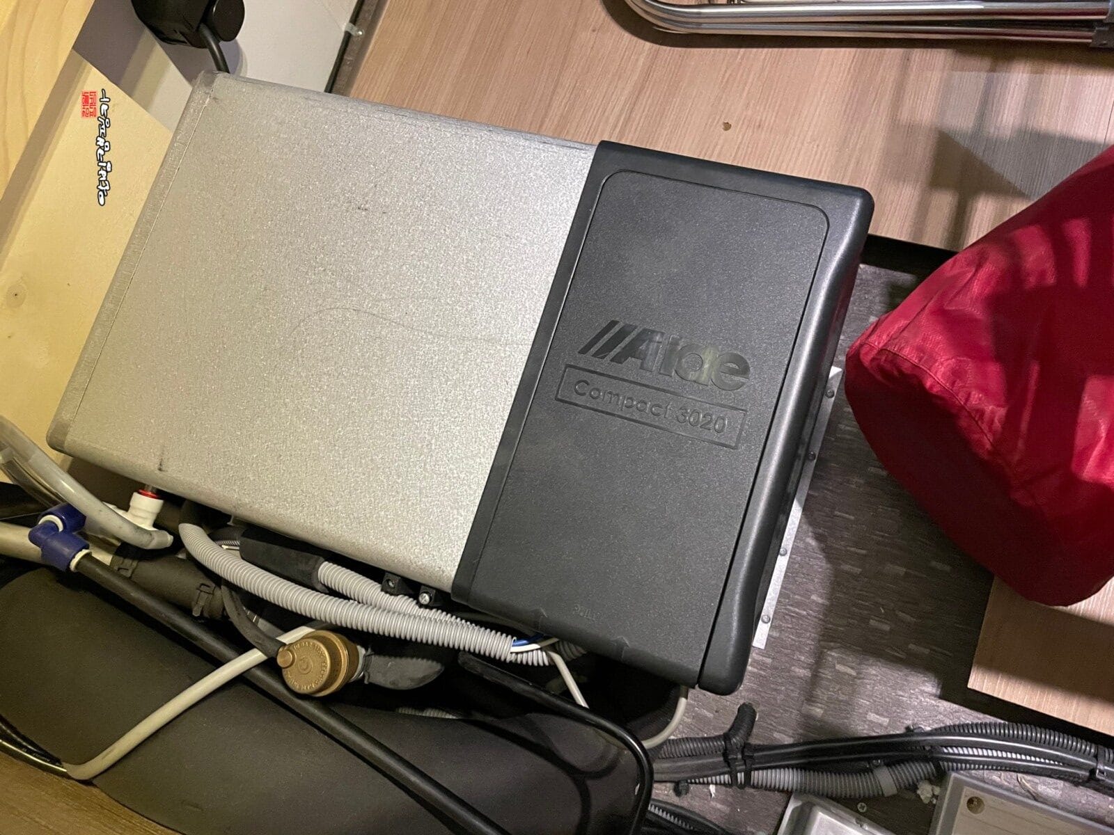 카라반 침대 하단 수납장 내부에 설치되어 있는 은색 바디와 검은색 커버의 알데(Alde) 컴팩트 3020 보일러 본체 모습